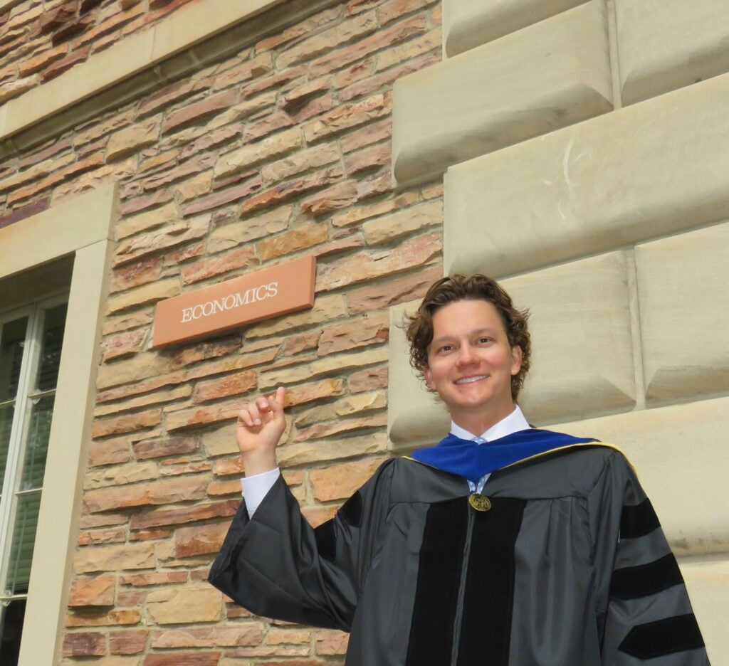 Michael Karas wearing a graduation gown and smiling.